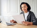 mulher-jovem-concentrada-revisando-documentos-com-laptop-em-uma-mesa-de-trabalho-brilhante (1)
